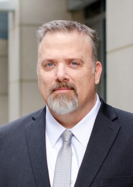 A picture of State Auditor Grant Parks in front of a building with a slight smile, grey hair middle-aged man